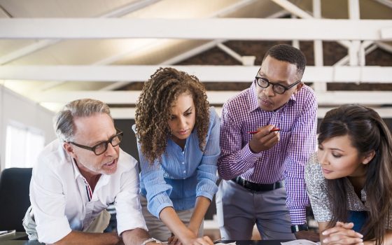 Multi-ethnic business people analyzing blueprint in creative office