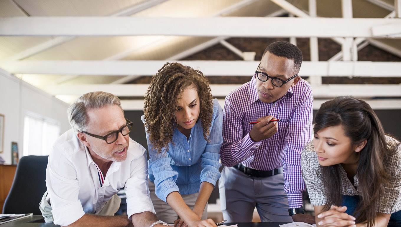 Multi-ethnic business people analyzing blueprint in creative office
