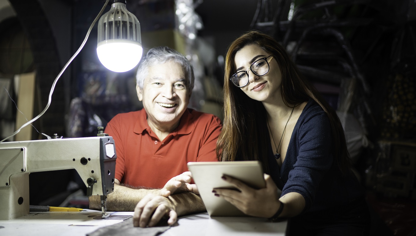 Man and woman in small office with sewing machine and tablet